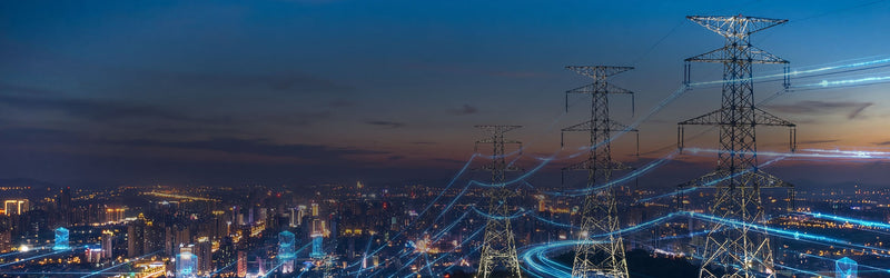 Cityscape at night with illuminated power lines and towers.